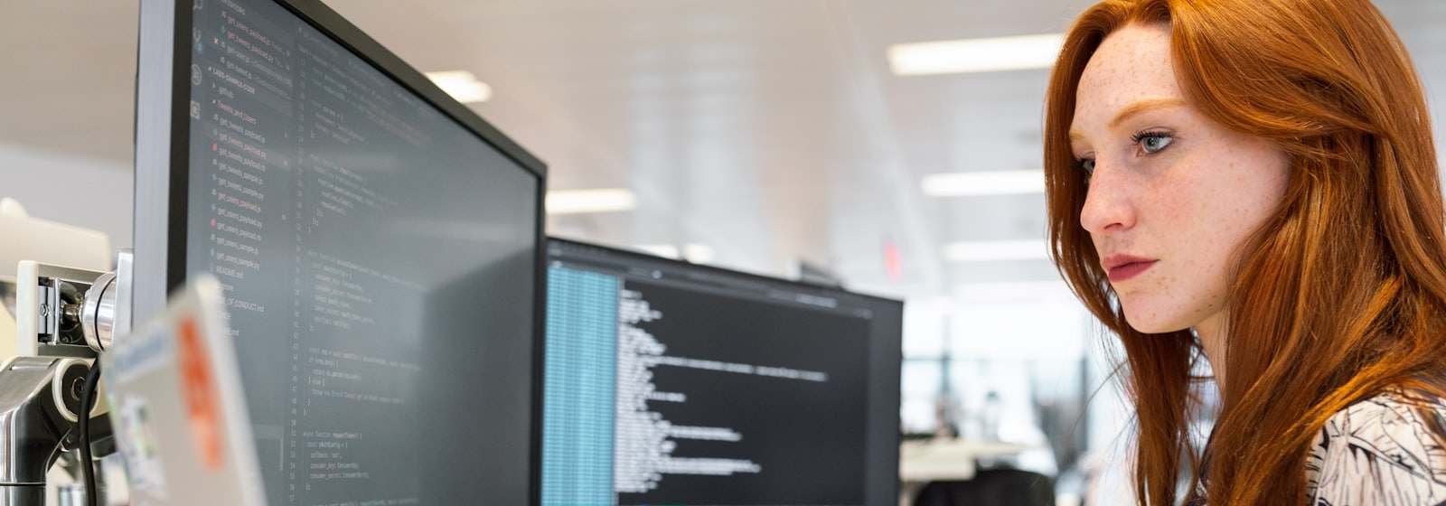 Een ontwikkelaar aan een bureau met twee monitoren vol code in een licht kantoor