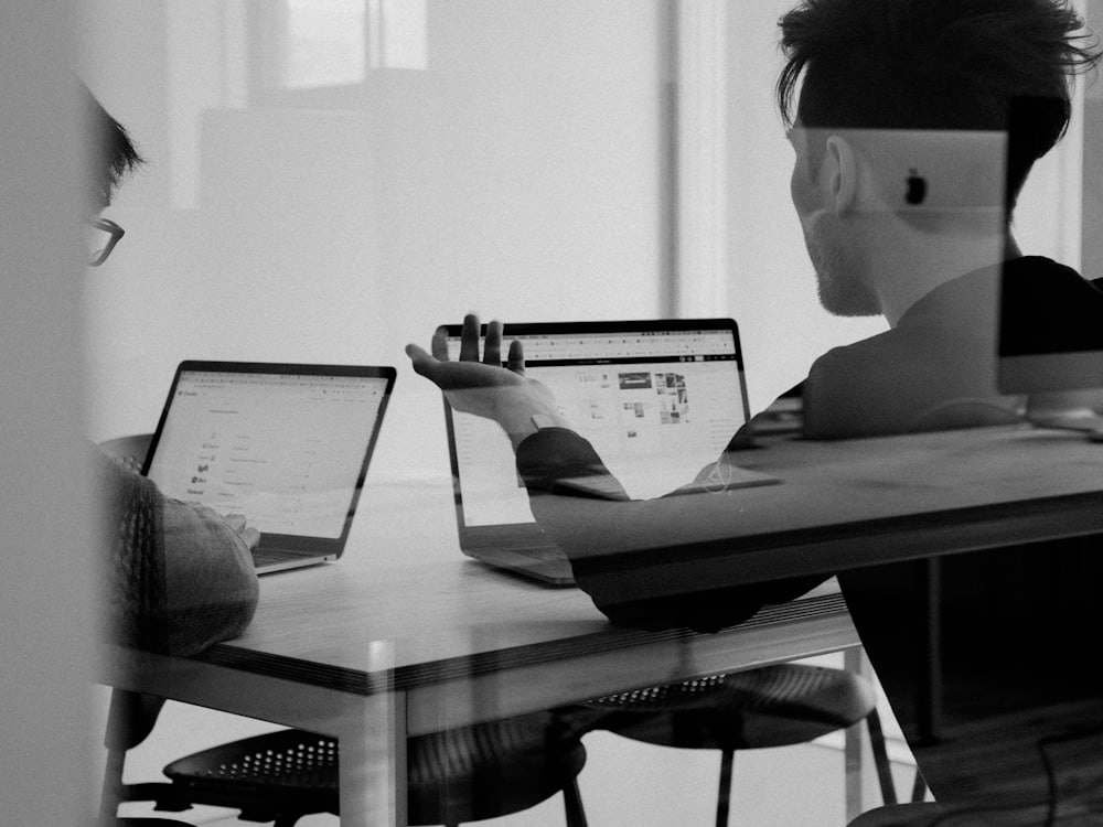 Dwie osoby rozmawiające nad laptopami, widziane przez szybę